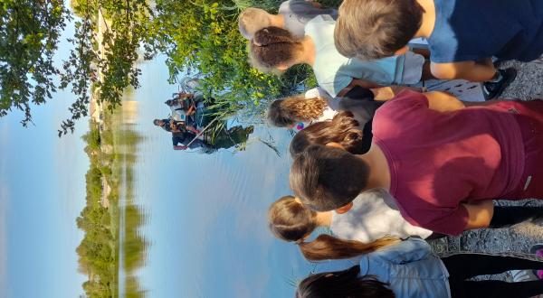 Groupe d'enfants devant un étang regardant une équipe de scientifiques sur un bateau 